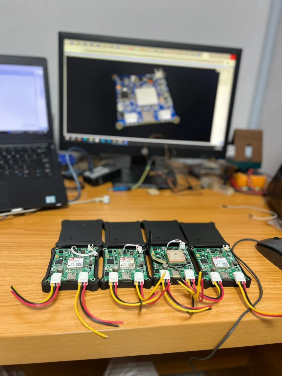 Finished tracking units in their enclosures, with the PCB design on screen